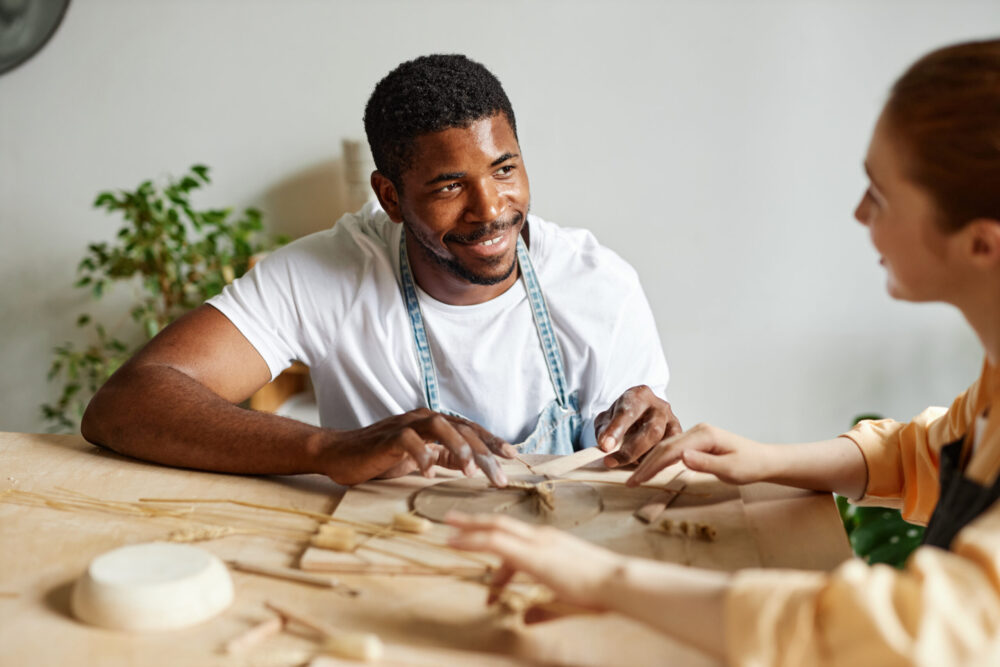 Portrait of young couple creating handmade ceramics together in pottery studio, copy space