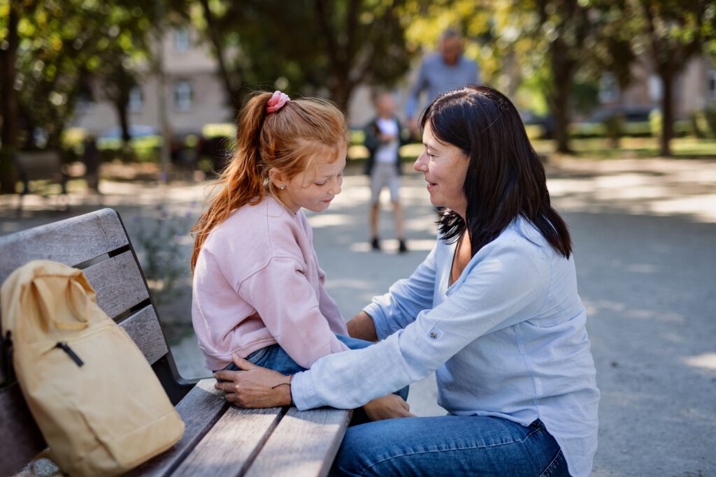 woman squatting and talking to a girl sitting on a bench