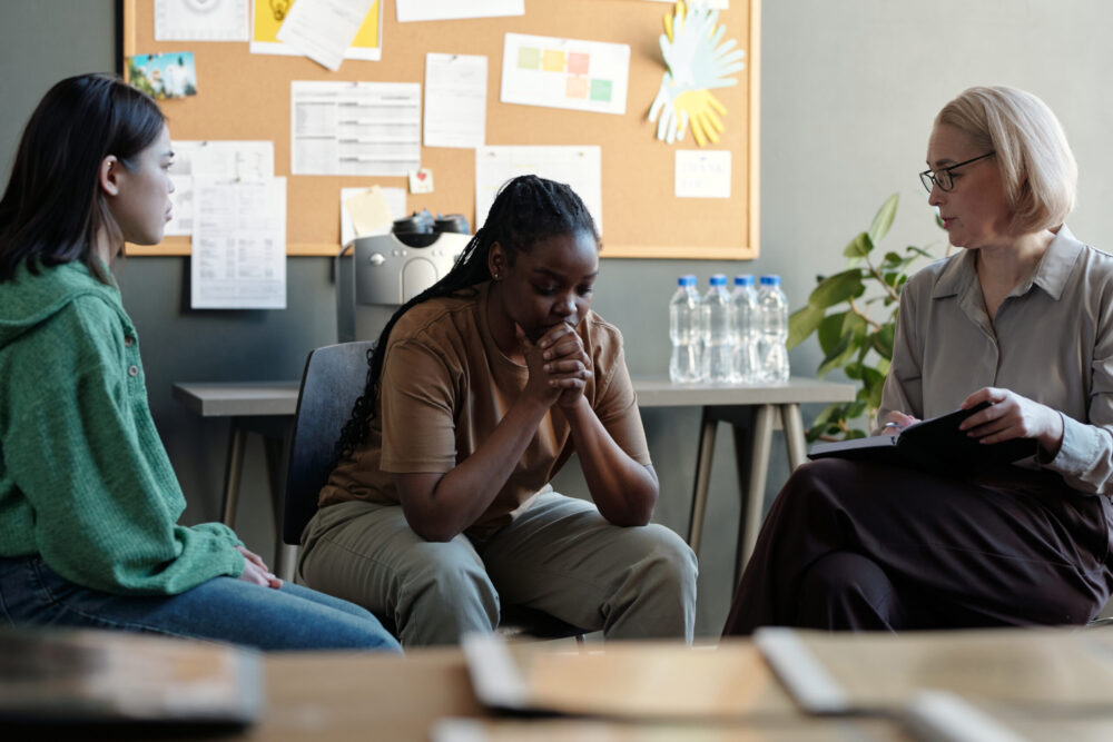 Young upset African American woman with post traumatic syndrome sitting among other people listening to her story during session